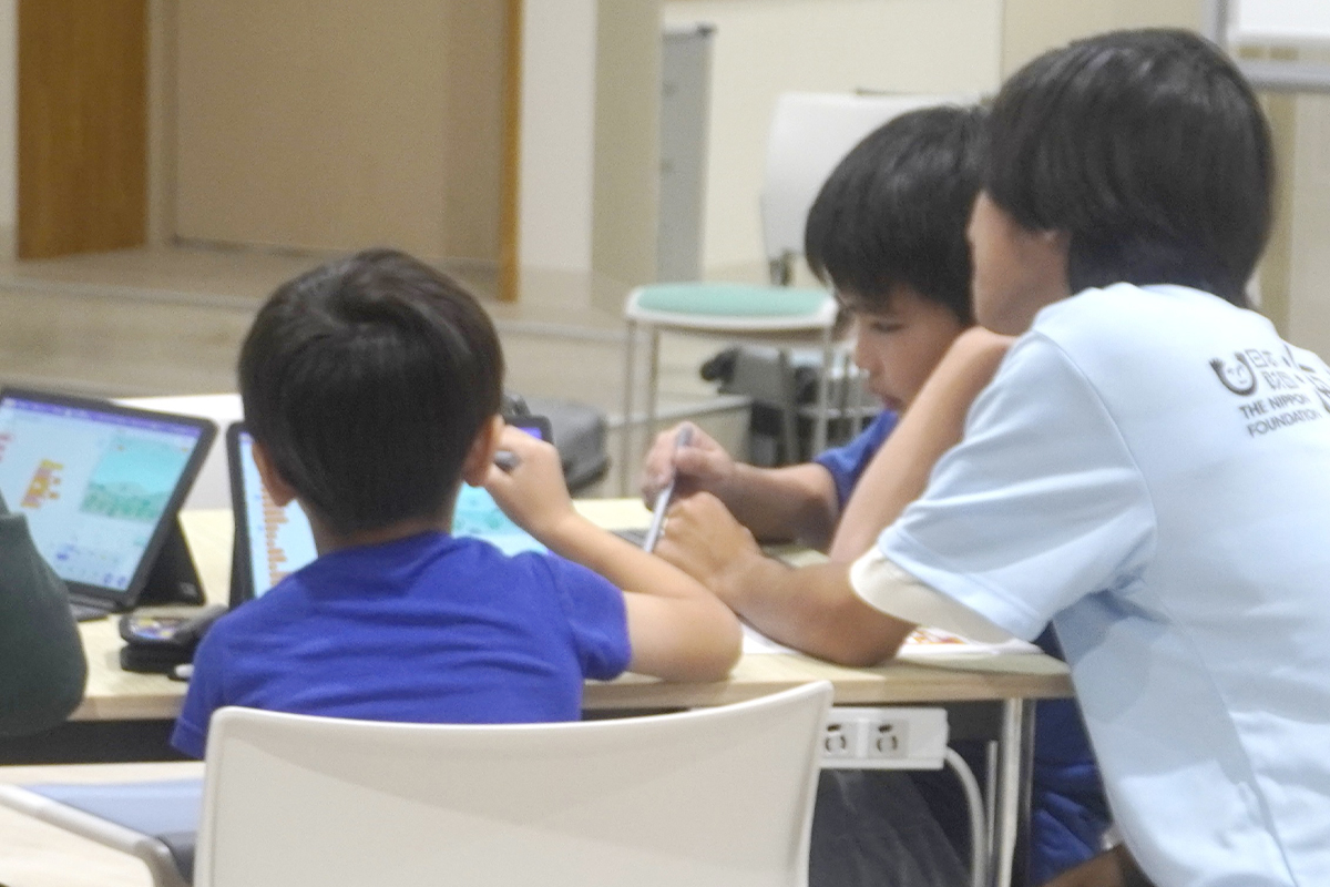 プログラミングをしている現地スタッフとこども達の後ろ姿